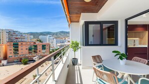 A balcony with a table and chairs, a potted plant, and a view of buildings and mountains.