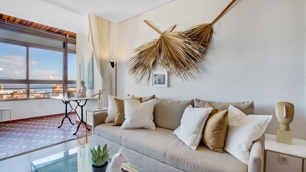 A modern living room with a sofa, a coffee table, and a view of the city through large windows. - Casa Lawrence - Sea Views (Torremolinos)