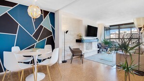 A modern living room with a geometric wall design, a fireplace, a flat-screen TV, and a view of the city. - Casa Lawrence - Sea Views (Torremolinos)