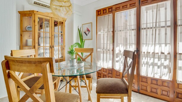 Un coin repas comprenant une table en verre, des chaises en bois, un buffet en bois et une grande fenêtre avec des rideaux.