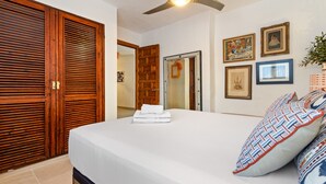 Une chambre avec un grand lit, une armoire en bois, un ventilateur de plafond et des tableaux encadrés accrochés au mur.
