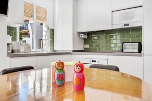 A modern kitchen with white cabinets, a green backsplash, and a wooden dining table with two colorful matryoshka dolls.