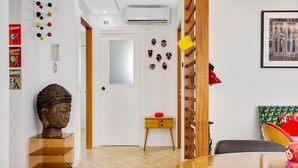 A modern living room with a wooden dining table, a Buddha statue on a glass cabinet, a small wooden side table with a red object, and a colorful chair. - Casa Fandango - Pueblo Blanco (Torremolinos)