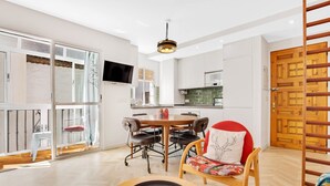 A modern kitchen with white cabinets, a wooden dining table, and a TV mounted on the wall. - Casa Fandango - Pueblo Blanco (Torremolinos)