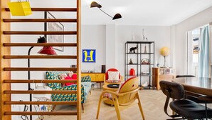 A modern, well-lit room with a wooden slat partition, a desk with a chair, a bookshelf, and a bed with colorful bedding. - Casa Fandango - Pueblo Blanco (Torremolinos)