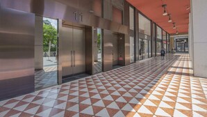 A hallway with a checkered floor, elevators, and a red ceiling. - Sweett | Central Tower III (Milano)