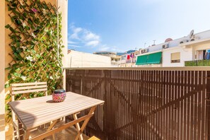A wooden table and bench on a balcony with a bamboo fence and climbing plants.