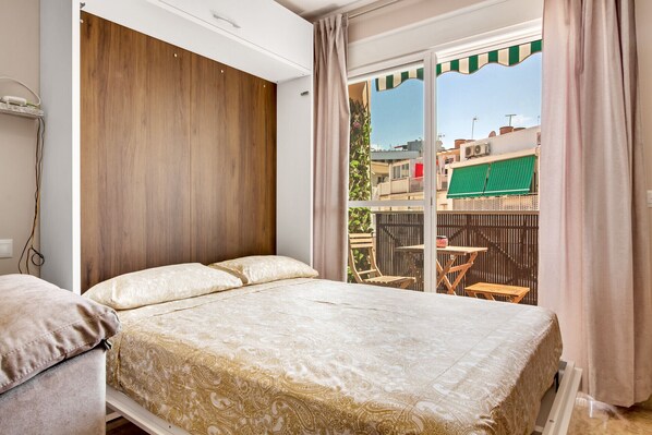 Une chambre avec un grand lit, une armoire en bois et un balcon aménagé avec du mobilier d’extérieur.