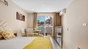 Een hotelkamer met een bed, een tafeltje, stoelen, een balkon met uitzicht op de stad en een airconditioning.