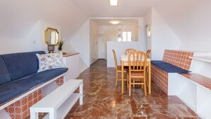 Una sala de estar moderna con un sofá azul, una mesa de comedor con sillas y una escalera que sube a otro nivel.