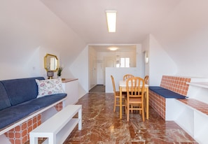 A modern living room with a blue sofa, a dining table with chairs, and a staircase leading to another level.