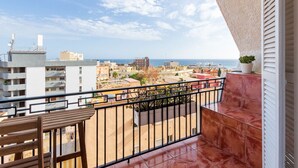 Un balcón con una mesa y sillas de madera, una planta en maceta y vistas de una ciudad costera.