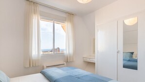 Un dormitorio con cama, ventana con cortinas, mesita de noche y espejo en la pared.