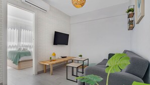 A modern living room with a grey sofa, a wooden coffee table, a TV mounted on the wall, and a large window with sheer curtains. - Casa Lido - Front line beach (Torremolinos)
