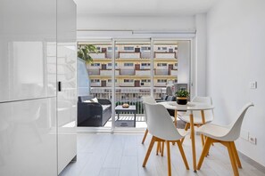 Un appartement moderne doté d’un balcon, de meubles blancs et offrant une vue sur un immeuble d’habitation.