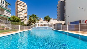 A swimming pool with a white fence, surrounded by buildings and palm trees. - Casa Lido - Front line beach (Torremolinos)