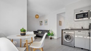 A modern kitchen with a built-in washing machine, a dining area with white chairs and a table, and a gray sofa in the background. - Casa Lido - Front line beach (Torremolinos)