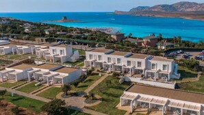 A coastal resort with modern white villas, a beach, and clear blue waters.