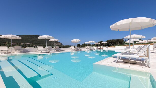 A clear blue pool with white lounge chairs and umbrellas, surrounded by a hilly landscape.