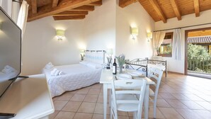 A bedroom with two beds, a dining table with chairs, a bathroom with a mirror, and a balcony with a view of greenery.