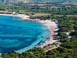 Vue aérienne d’une zone côtière avec une plage, une côte rocheuse et une végétation luxuriante environnante.