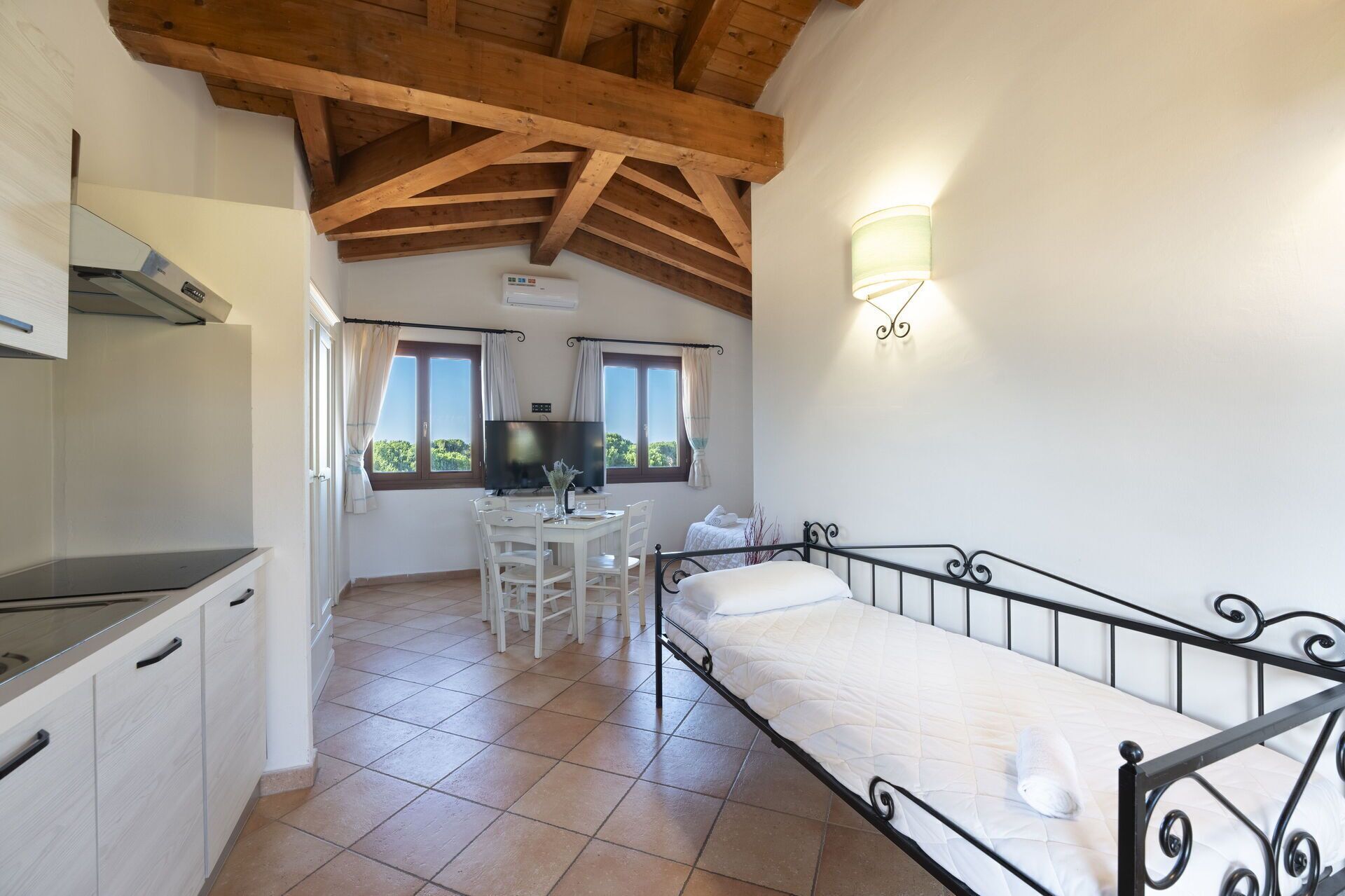A compact room with a bed, kitchenette, dining area, and a TV.
