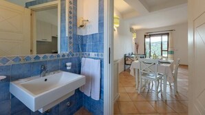 A bathroom with a sink, mirror, and blue-tiled walls. There is a dining area with a table and chairs visible through an open door. - Onda Apartment Ac Wifi, Gallura (Portobello Di Gallura)