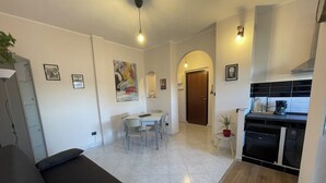 Un salon moderne avec un canapé, un coin repas avec des chaises, une cuisine équipée d’une cuisinière et un couloir avec une porte.