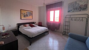 Une chambre à coucher avec un lit, un bureau, une chaise, une fenêtre avec des rideaux et un tableau au mur.