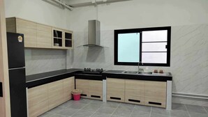 A modern kitchen with a black countertop, wooden cabinets, a stainless steel sink, and a window with a view. - Modern House CNX (Chiang Mai)