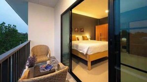 A bedroom with a bed, a chair, and a table on a balcony with a view of greenery. - Modern House CNX (Chiang Mai)