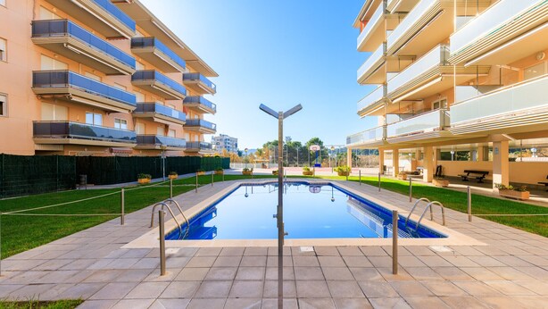 Une piscine avec un poteau métallique au centre, entourée d’une allée dallée.