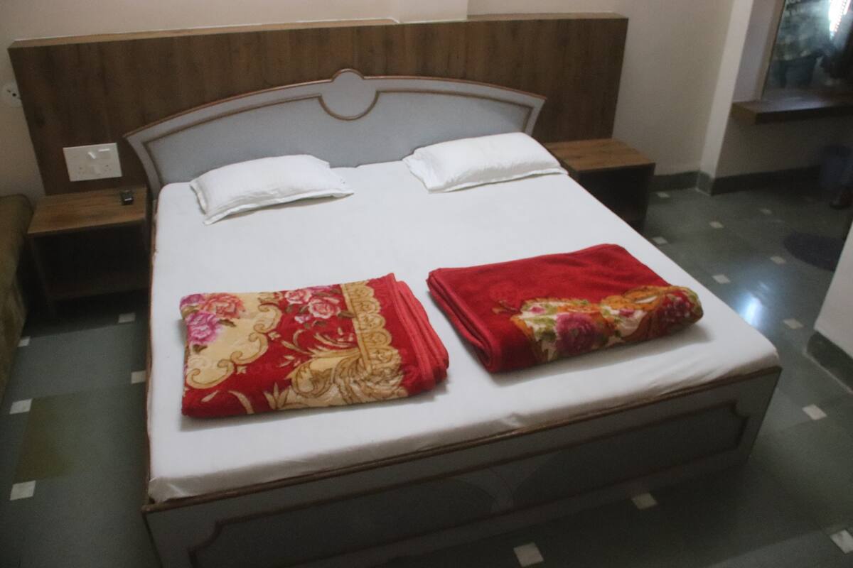 A bed with a wooden headboard, white bedding, and two red blankets.