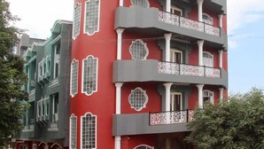 Un edificio de varios pisos con fachada roja, detalles decorativos blancos y balcones con barandillas ornamentales.