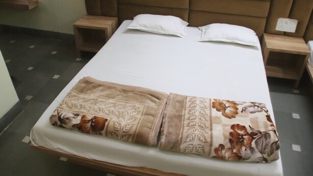 Un lit simple avec une couverture à motifs floraux, deux oreillers et une tête de lit. Il y a deux tables de chevet, chacune avec une lampe. La pièce a un sol carrelé et un mur uni.