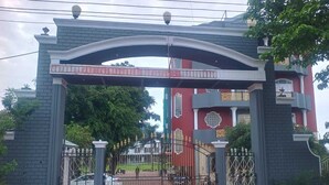 Una entrada con reja y un arco decorativo que conduce a un edificio de fachada roja y un balcón.