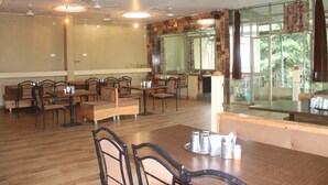 Un comedor con varias mesas y sillas, un ventanal con cortinas y ventiladores de techo.