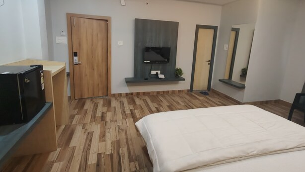 Una habitación de hotel moderna con suelo de madera, una cama, un televisor en la pared, un escritorio con computadora y un espejo.