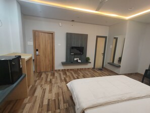 Une chambre d’hôtel moderne avec un plancher en bois, un lit, un téléviseur fixé au mur, un bureau avec un ordinateur et un miroir.
