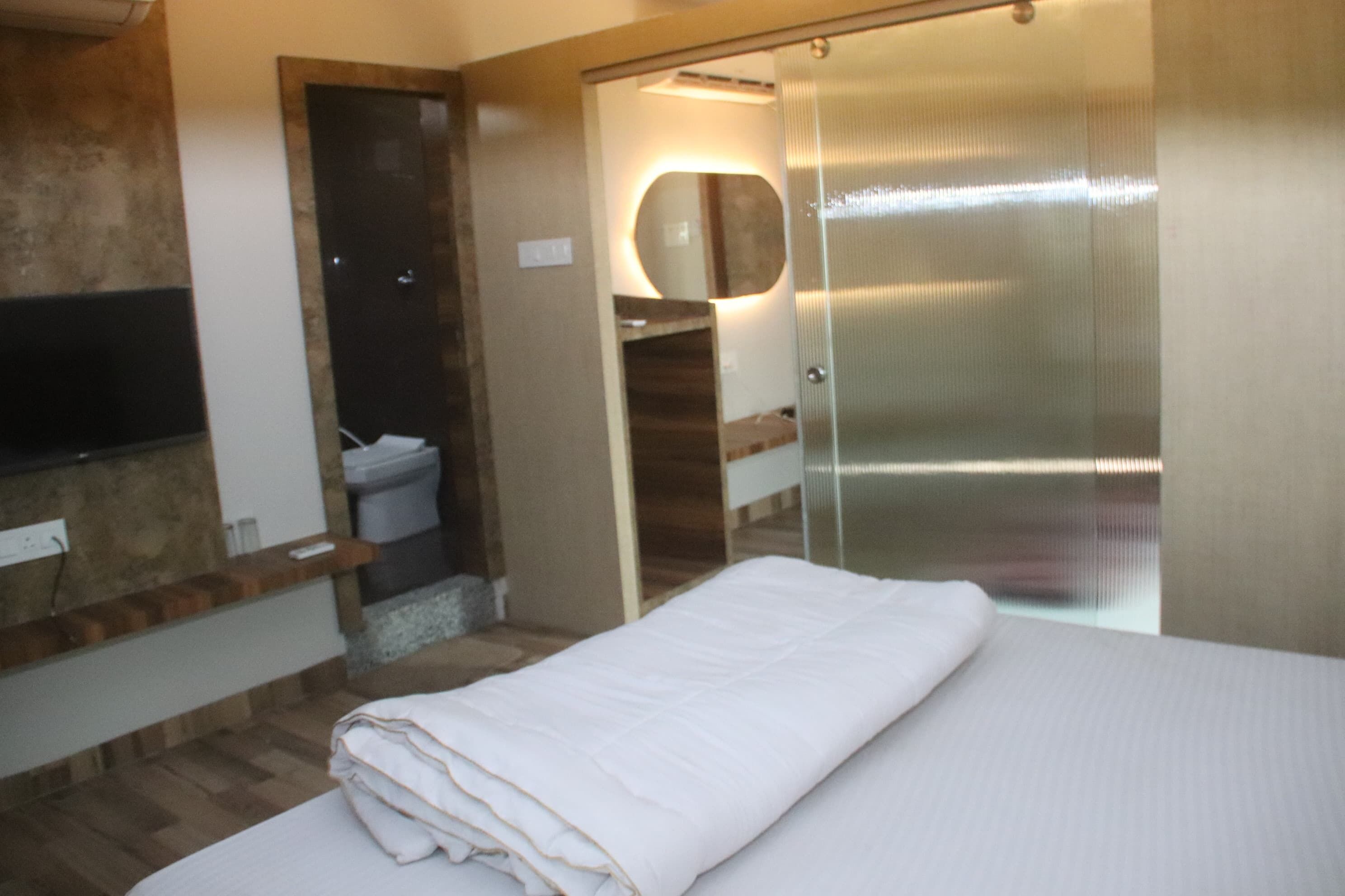 A hotel room with a bed, a bathroom with a toilet and sink, a mirror, and a TV mounted on the wall.