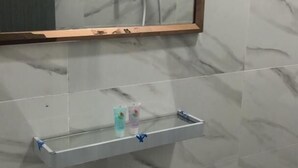 Un baño con un lavamanos blanco, un grifo negro, un espejo con marco de madera y un cabezal de ducha sobre el espejo.
