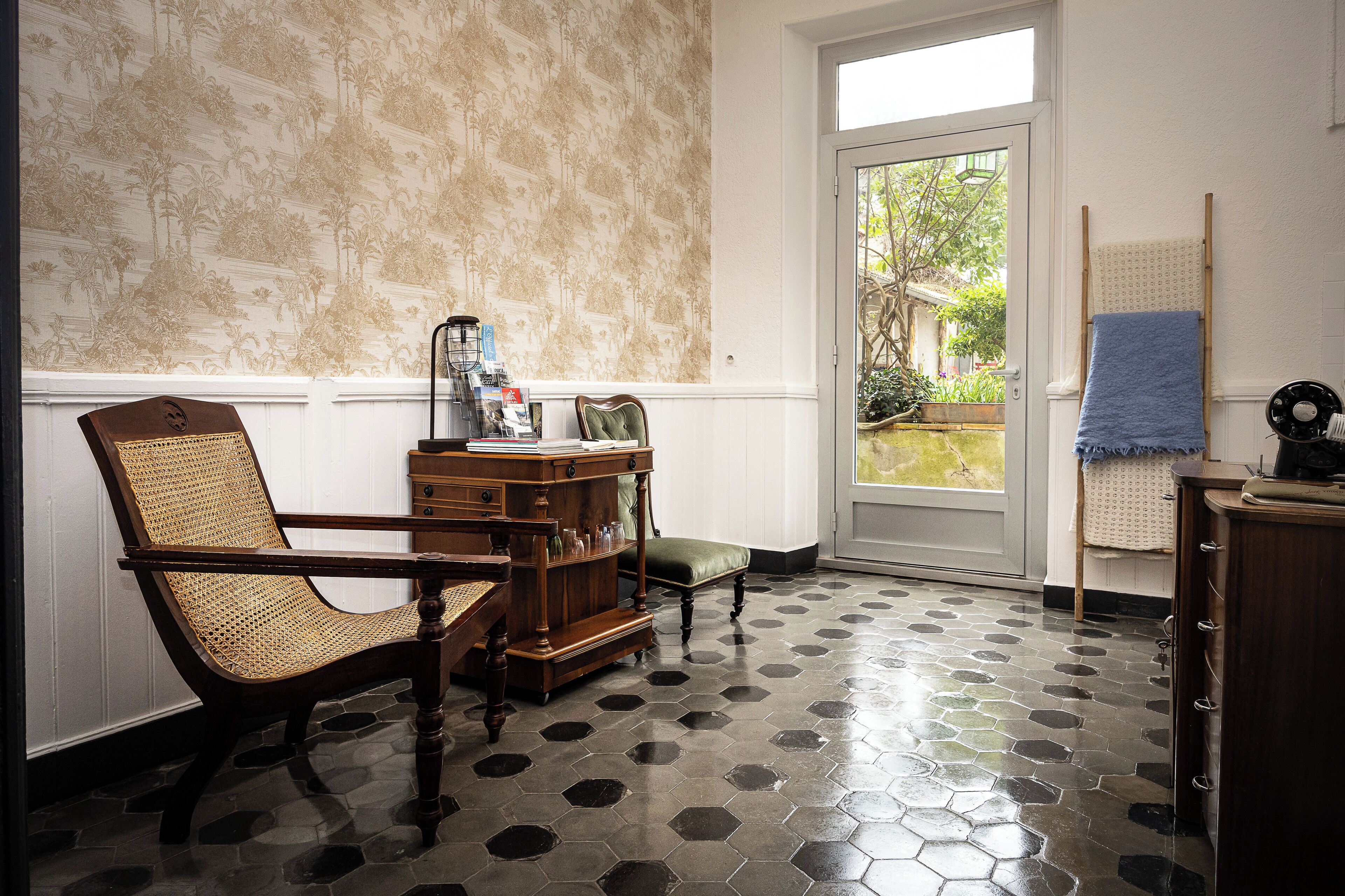 Una habitación con piso de baldosas hexagonales, una silla de madera, un armario de madera y una puerta que da al exterior.