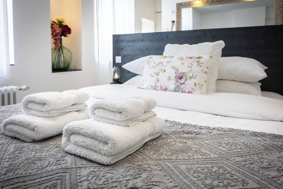 Un lit bien fait, avec des serviettes pliées, un coussin à motifs floraux et un tapis à dessins.