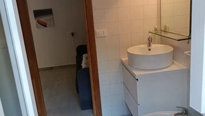 Une salle de bain avec un lavabo blanc, une étagère en verre et un miroir.