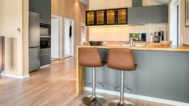 Une cuisine moderne avec un lambris en bois, un îlot central doté de tabourets de bar et un four encastré.