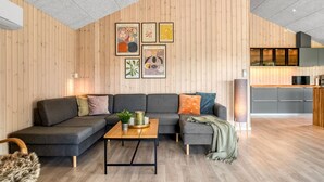 Un salon moderne avec un canapé d’angle, une table basse en bois et une cuisine en arrière-plan.