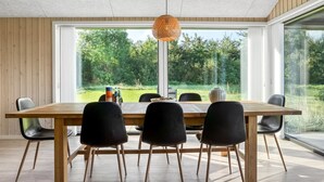 Un espace repas comprenant une grande table, quatre chaises et un luminaire suspendu.
