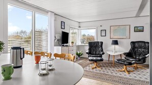 Een ruime woonkamer met een eettafel, twee leren fauteuils, een salontafel en een televisie.