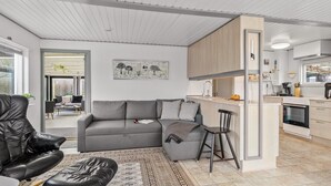 Een moderne woonkamer met een grijze bank, een zwarte lederen fauteuil en een kamerkleed met een patroon.