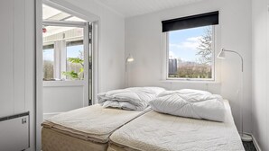 Een slaapkamer met een bed, twee bedlampjes, een raam met uitzicht op groen en een radiator.
